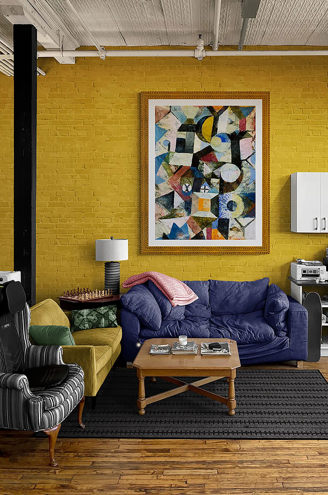 A vibrant livingroom with yellow brick wall and an oversized framed art print by Paul Klee.